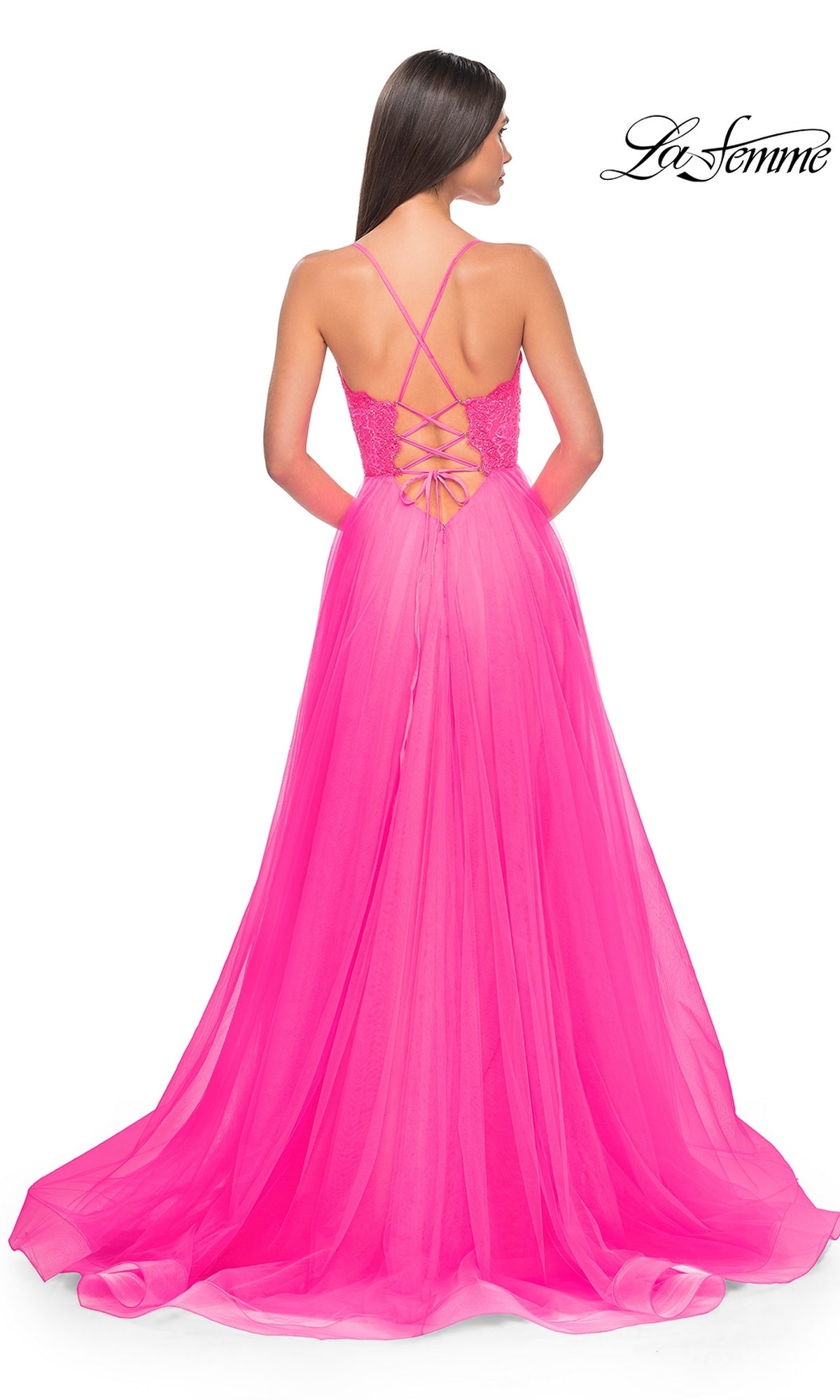A woman in the La Femme Lace-Bodice Long A-Line Prom Dress 32306, a bright pink gown with a lace-up back, crisscross straps, and a flowing sheer floor-length skirt for an elegant statement.